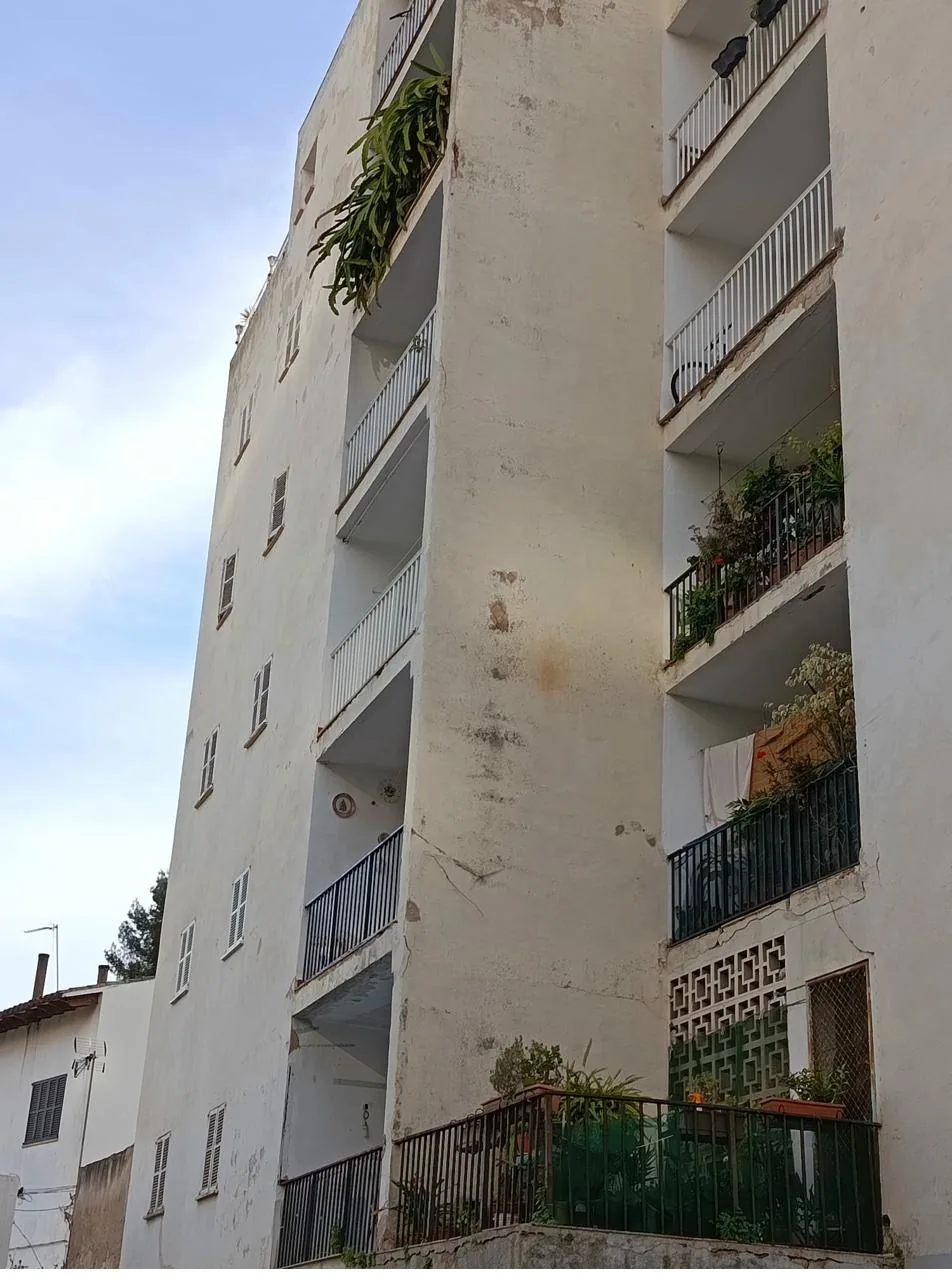 Fachada de edificio en Mallorca con manchas verticales de humedad bajo canalón obstruido por falta de mantenimiento periódico