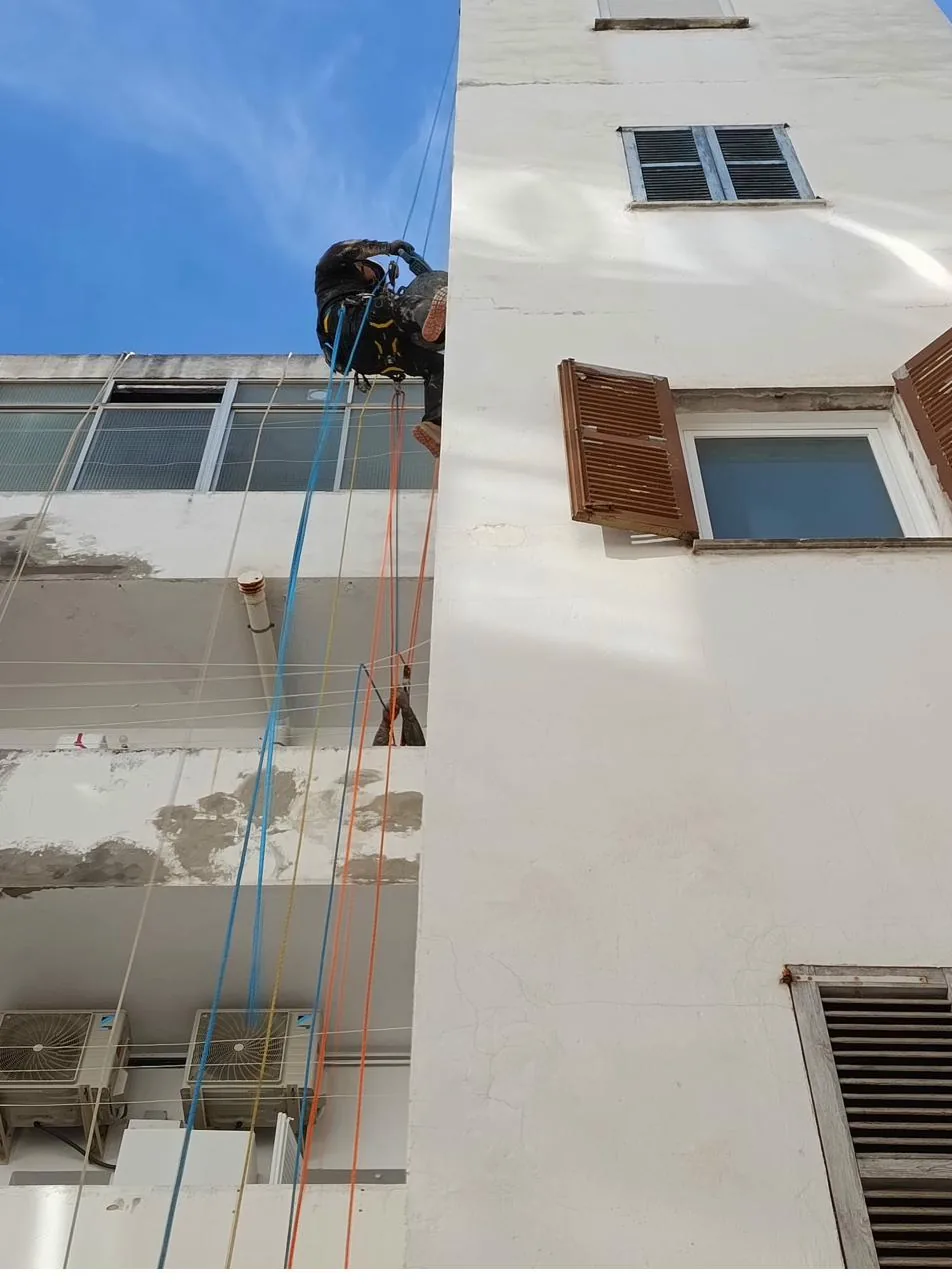 Vertical reparando cornisa en fachada de comunidad de Capdepera desde cuerda