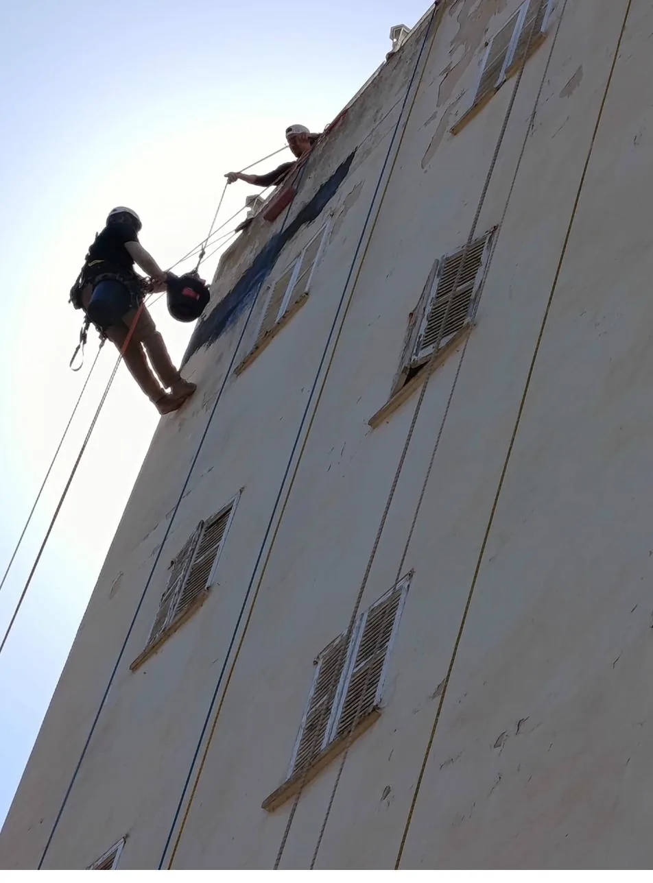 Vertical de Roca Verticales pintando una fachada amarilla descascarillada en Palma sin andamio