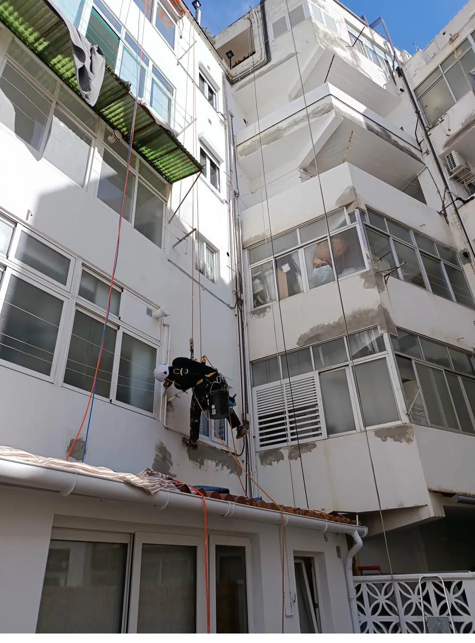 Vertical de Roca Verticales aplicando pintura con rodillo profesional sobre fachada saneada en Mallorca
